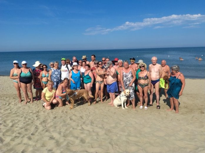 Foto di gruppo dei soci in spiaggia insieme ai due cani guida.